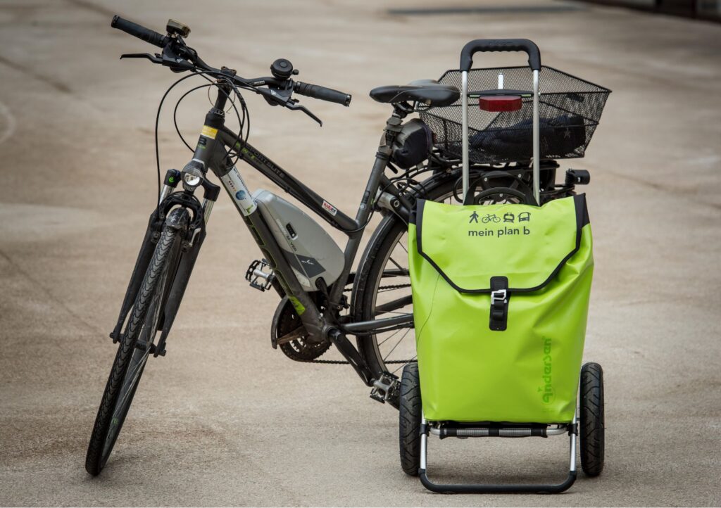 Abgestelltes Fahrrrad, davor steht ein grüner Trolly mit einem plan-b-Logo