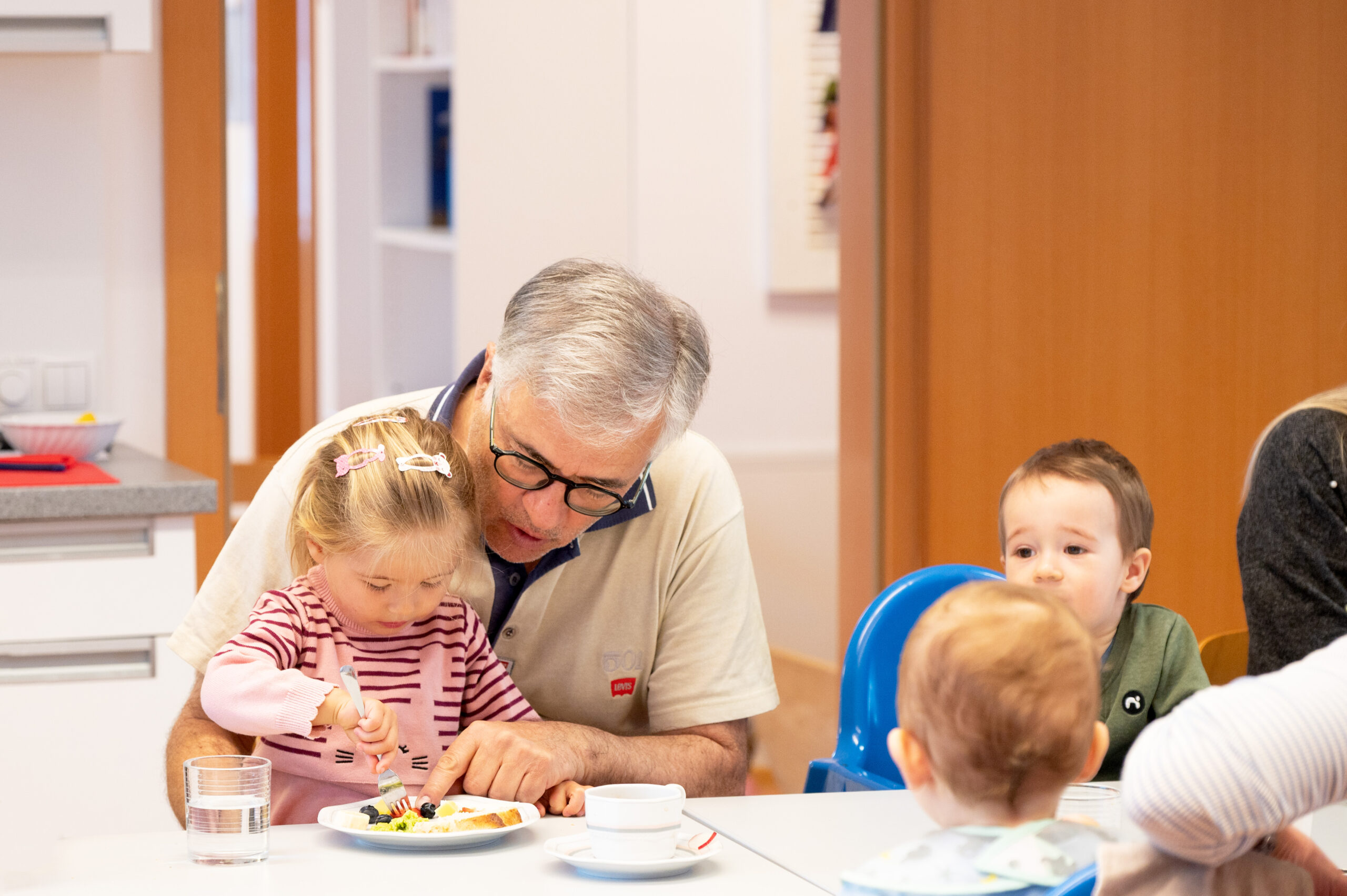 Ein Mann sitzt mit einem Mädchen an einem gedeckten Frühstückstisch und zeigt auf das Essen.