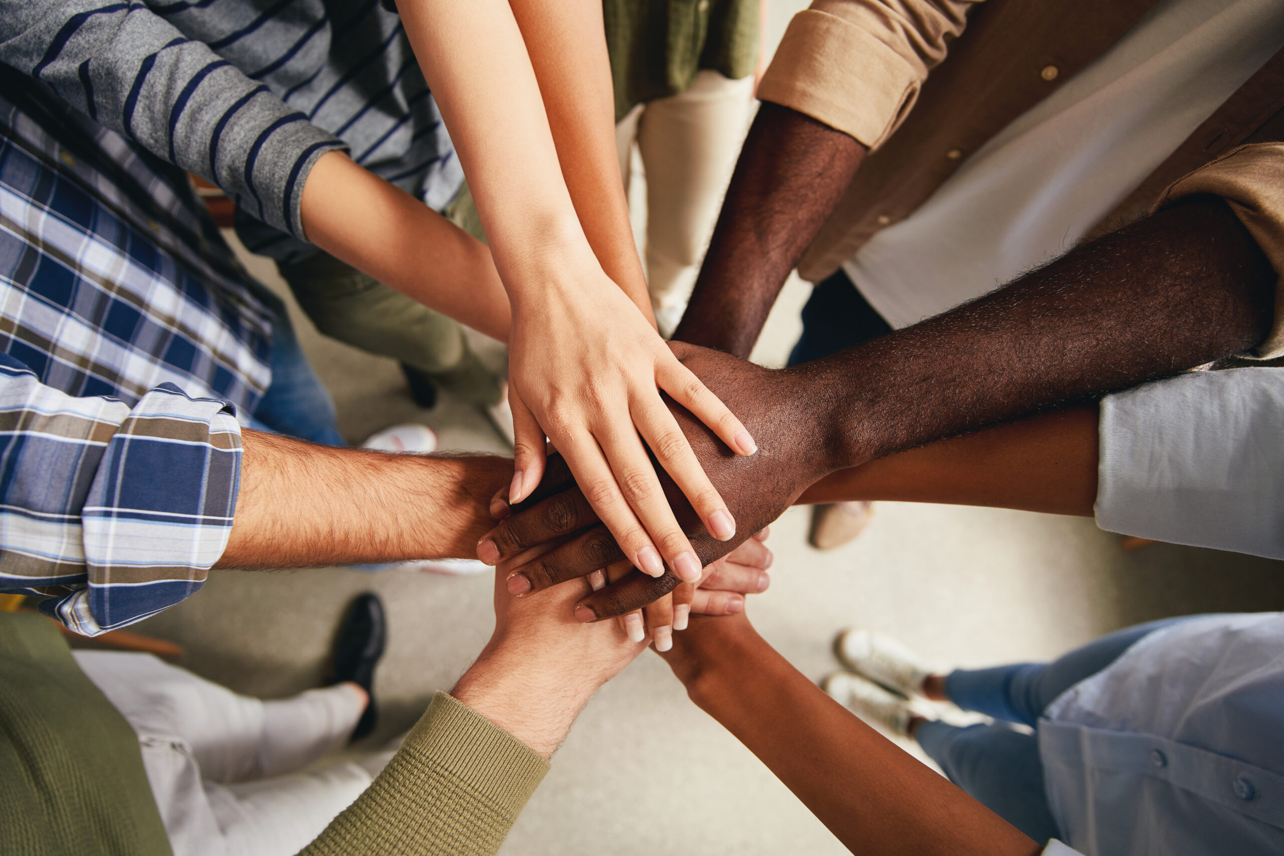 Mehrere Menschen unterschiedlicher Herkunft legen ihre Hände übereinander – Symbol für Teamarbeit, Zusammenhalt und Vielfalt.