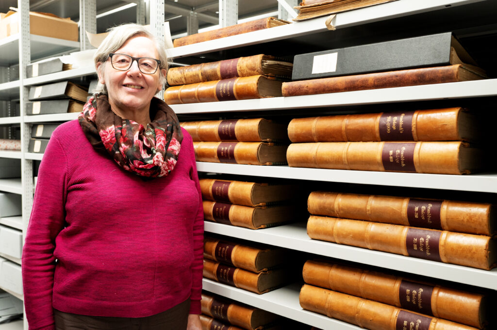 Das Bild zeigt Christine Schurr, die Gemeindearchivarin von Lauterach, die im Archiv vor einem Regal mit Büchern steht.