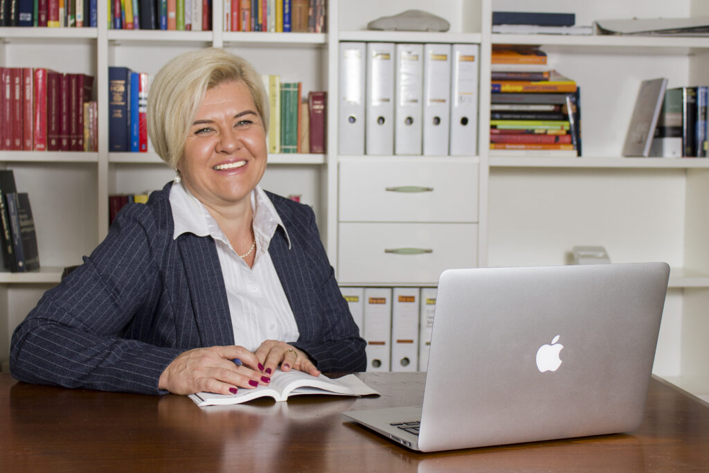 Das Bild zeigt Petra Dressel, die Vorsitzende des Ausschusses für Wohnungswesen der Marktgemeinde Lauterach. Sie sitzt in einem Büro vor einem Computer und lächelt in die Kamera.