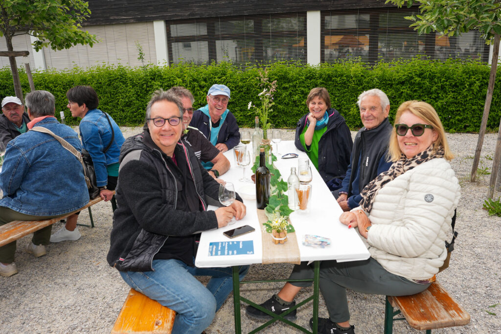 Das Bild zeigt eine Gruppe von acht Personen an einem weiß gedeckten Tisch im Freien. Sie trinken Wein und genießen das Fest in gemütlicher Atmosphäre.