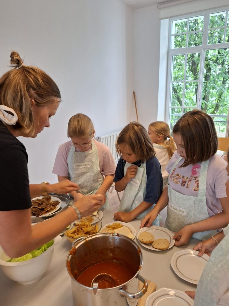 Das Bild zeigt eine Frau, die gemeinsam mit Kindern gesundes Essen kocht.