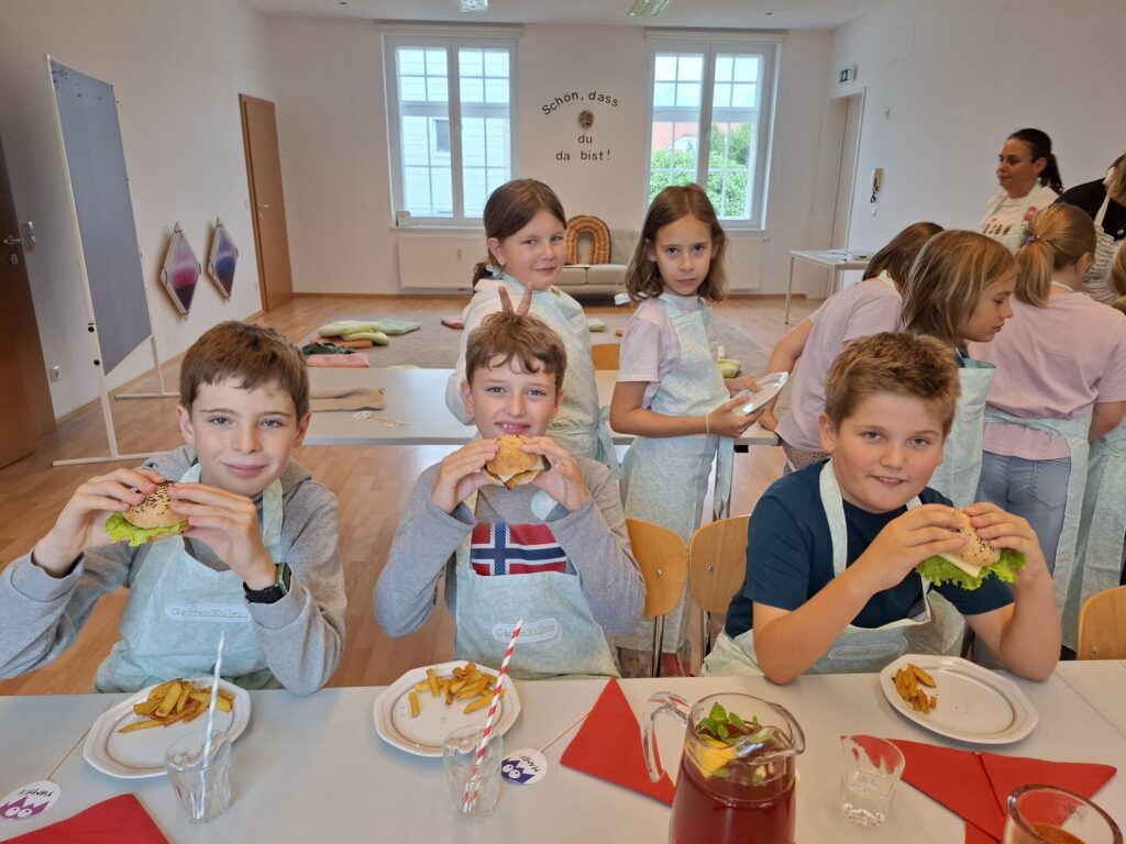 Das Bild zeigt drei Jungen, die in einen selbstgemachten, gesunden Burger beißen.