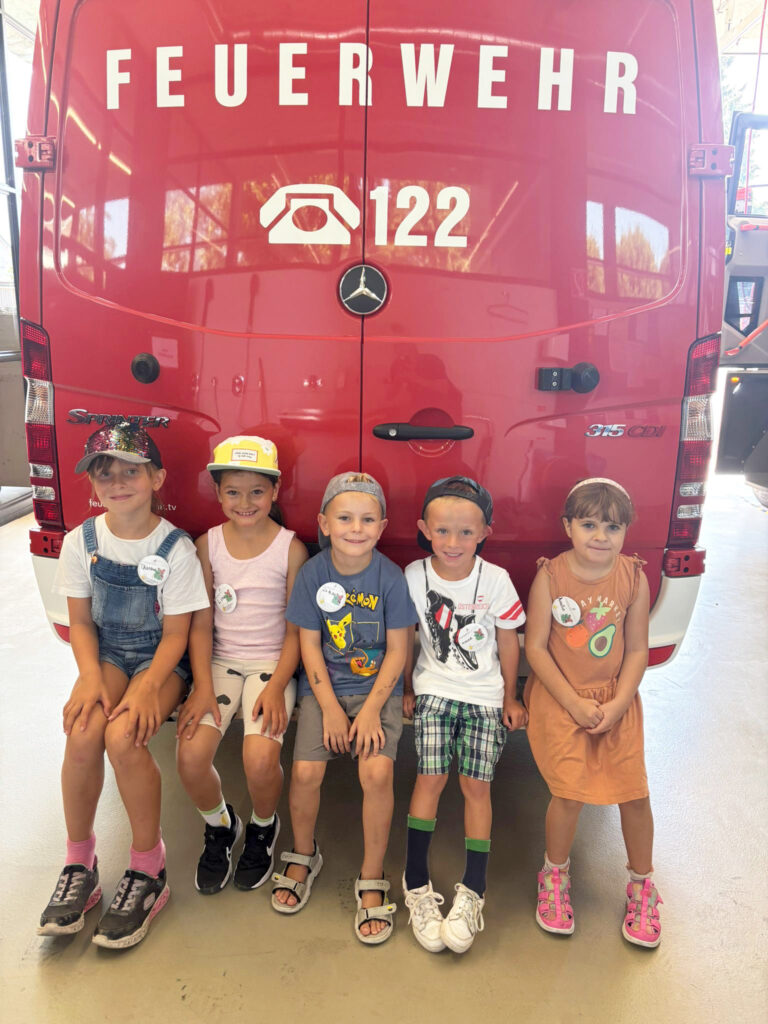 Das Kind zeigt fünf Kinder vor einem Feuerwehrauto.