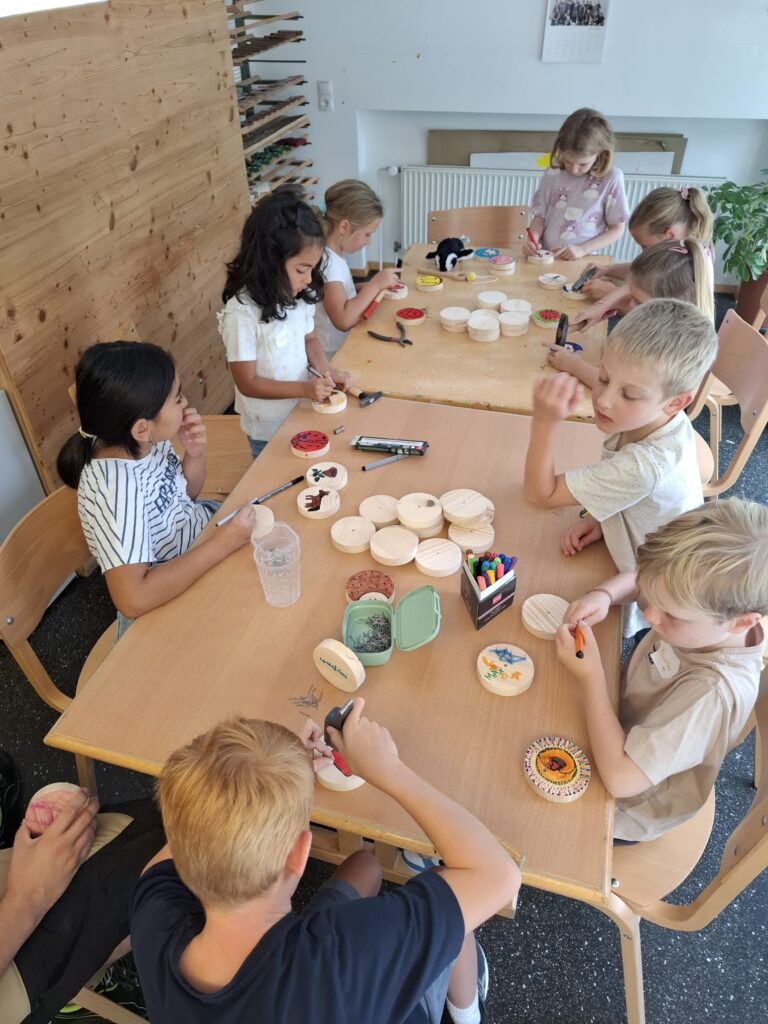 Das Bild zeigt eine Gruppe von Kindern an einem Tisch. Sie werkeln mit Holz.