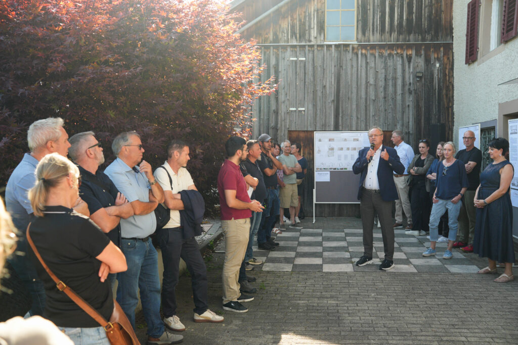 Das Bild zeigt Bürgermeister Elmar Rhomberg, der vor einer Gruppe Menschen vor dem Fesslerhaus steht und in ein Mikrofon spricht.