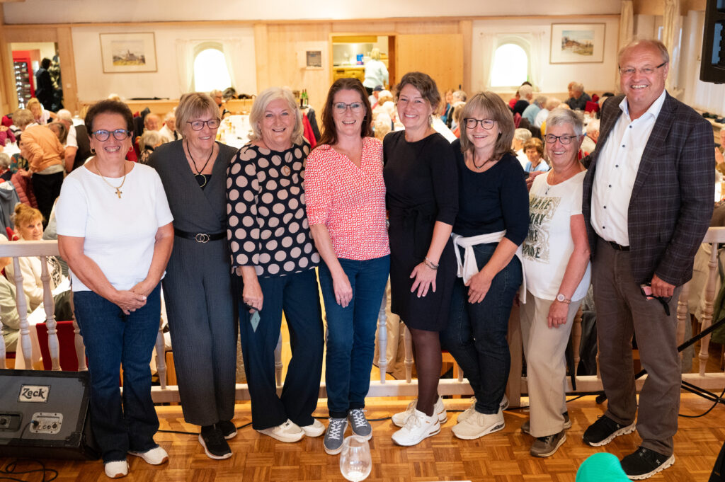 Das Bild zeigt Doris Rohner, Beatrix Springer, Katharina Pfanner, Margit Marik, Violetta Giselbrecht, Katharina Bilgeri, Evi Fetz und Bürgermeister Elmar Rhomberg, die lächelnd vor einer Festgesellschaft posiert.