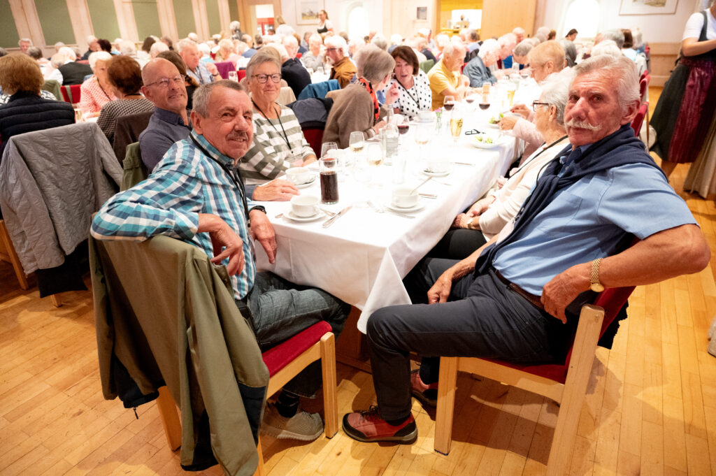 Das Bild zeigt mehrere Senior:innen, die gemeinsam an einem langen Tisch sitzen und sich unterhalten.