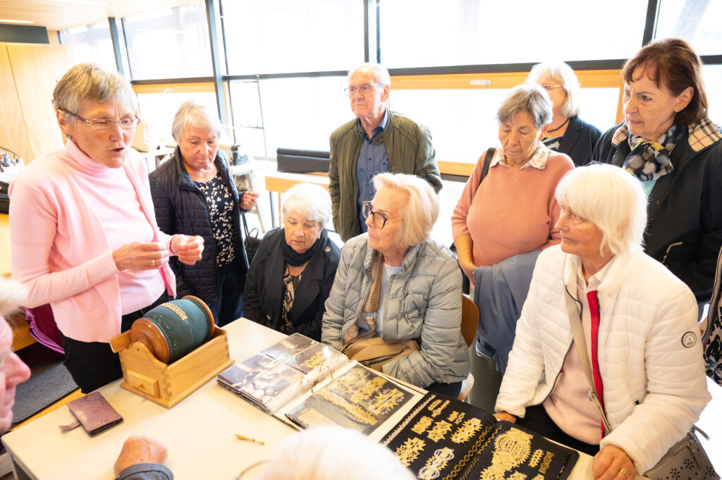 Das Bild zeigt eine Gruppe von Senior:innen, die sich eine Klöppelarbeit-Vorführung ansieht.