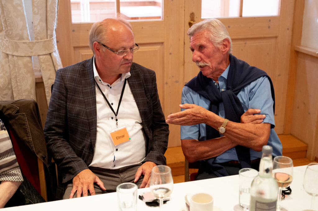Das Bild zeigt zwei Männer, die sich bei einem Festessen intensiv unterhalten.