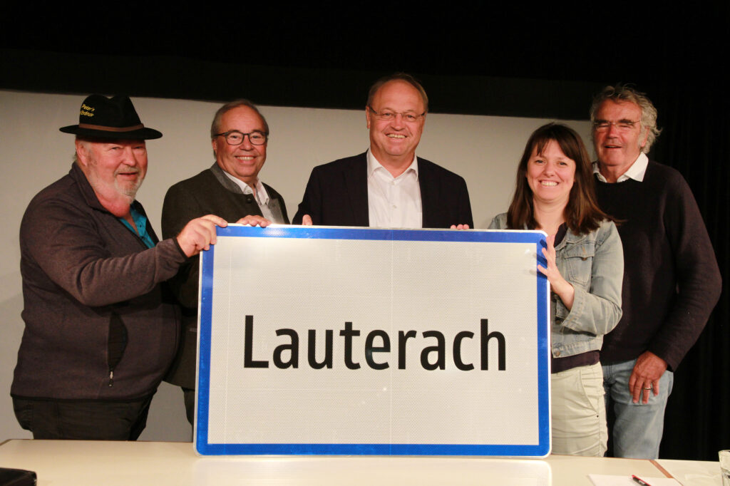 Das Bild zeigt Peter Dietrich, Walter Pfanner, Elmar Rhomberg, Sanda Alibegovic und Johannes Schmidle. Alle halten ein Lauterach Ortsschild in der Hand.