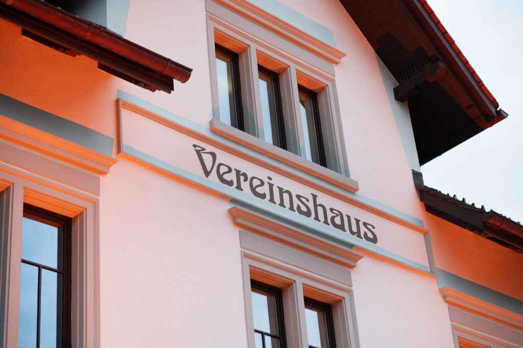 Das Bild zeigt das Vereinshaus in Lauterach am Abend, orange beleuchtet zu den Aktionstagen "Orange the World – 16 Tage gegen Gewalt an Frauen".