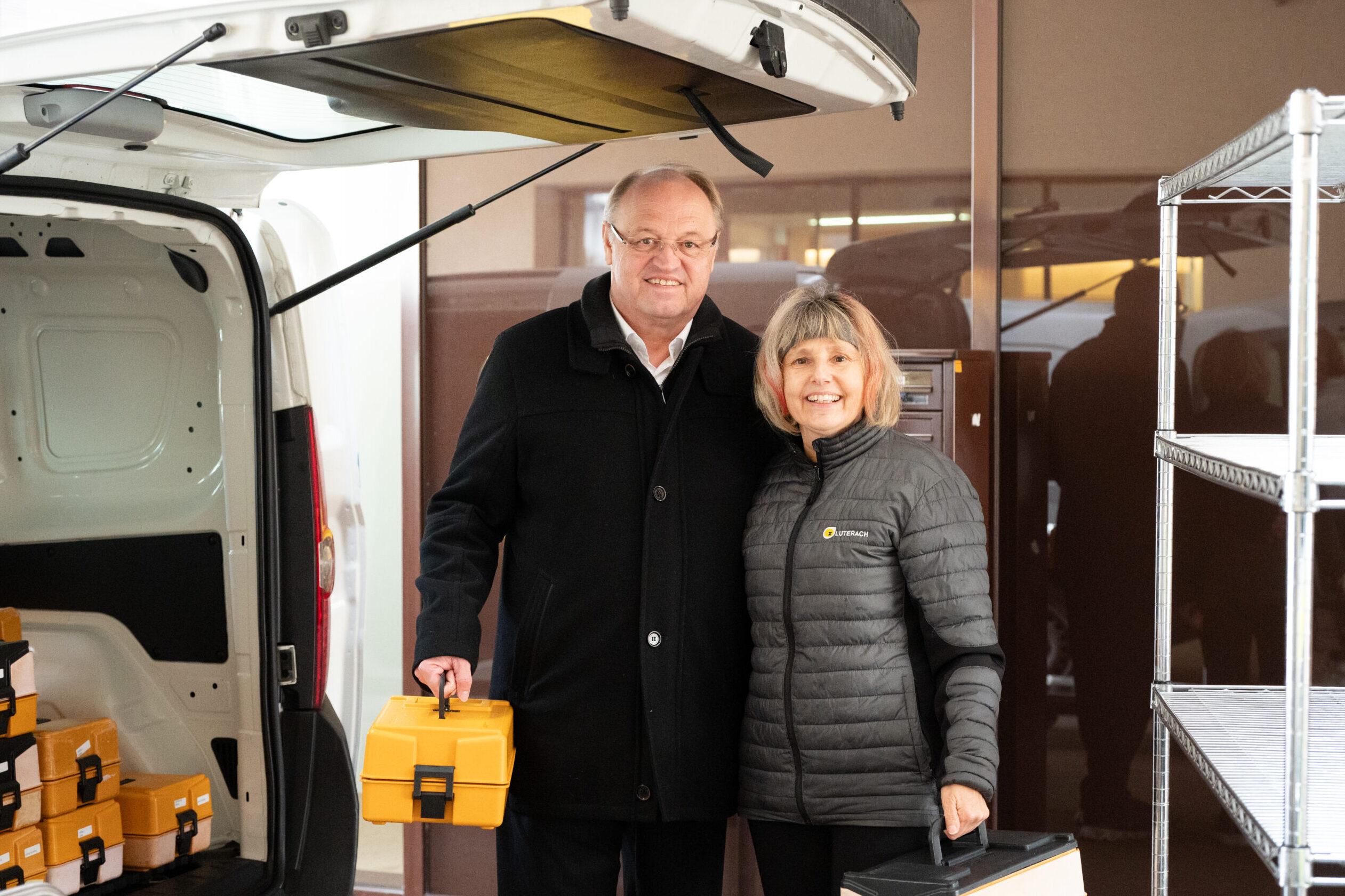 Das Bild zeigt den Bürgermeister Elmar Rhomberg gemeinsam mit einer Mitarbeiterin von "Essen auf Rädern" vor einem Auto bei der Weihnachtsausfahrt.