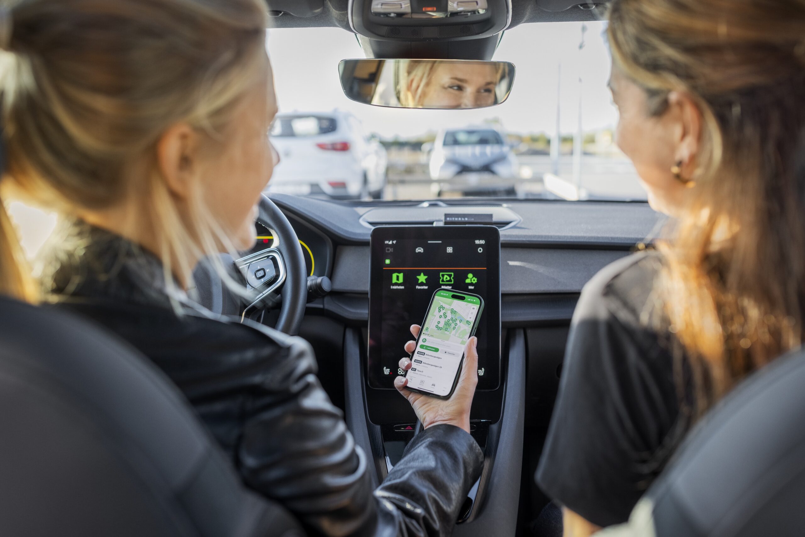 Das Bild zeigt zwei Frauen, die in einem Auto sitzen und auf einem Smartphone die App Parkster für Handyparken nutzen.