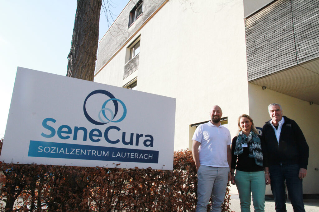 Auf dem Bild stehen Emanuel Jori (Hausleitung) und Helena Kussian (Hausinterne Pflegedienstleistung) vom SeneCura Sozialzentrum Lauterach und Moderator Johannes Schmidle vor einem Schild mit der Aufschrift "SeneCura Sozialzentrum".