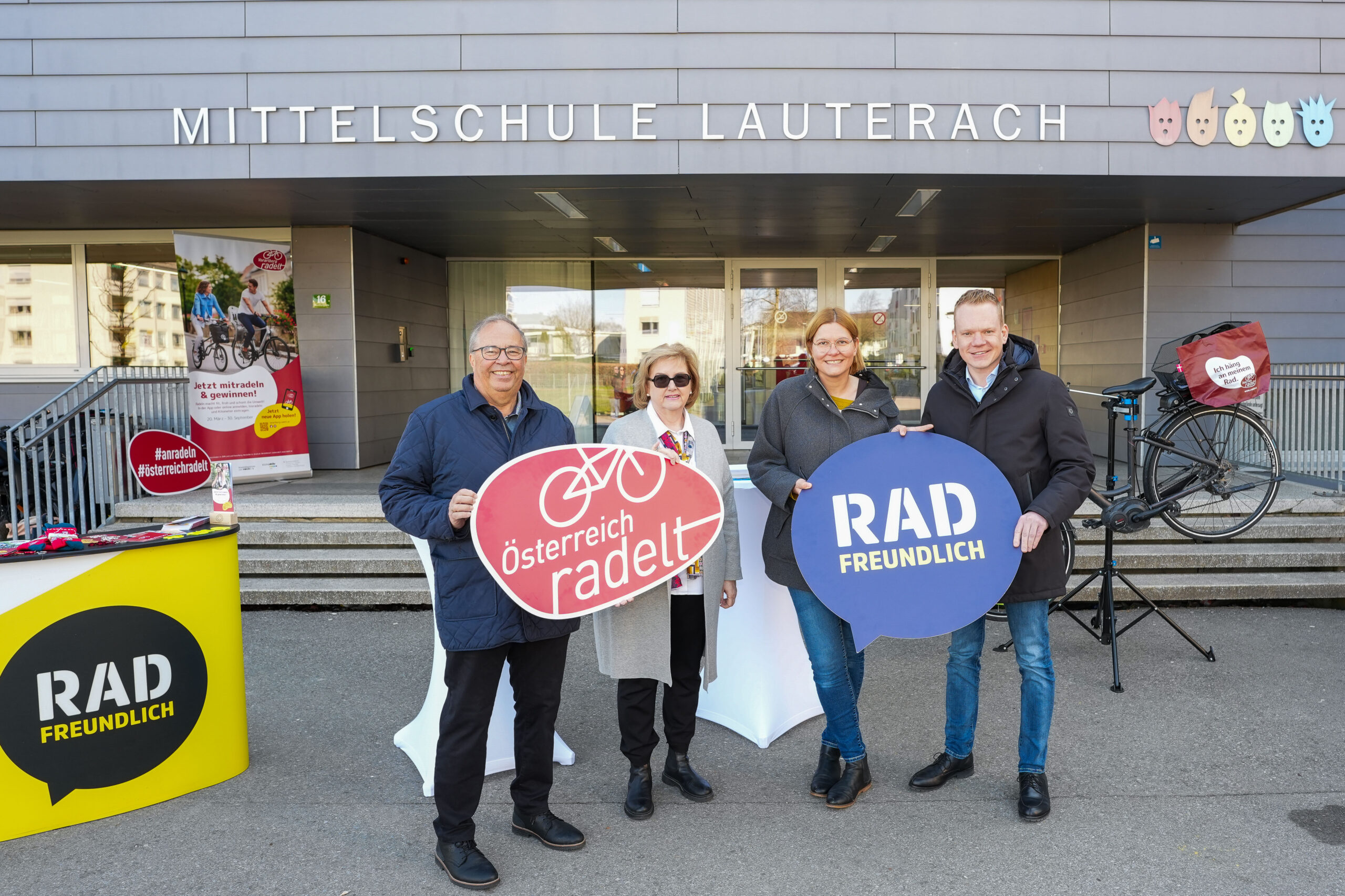 Das Bild zeigt eine Gruppe von Erwachsenen bei einem Pressetermin zu "Österreich Radelt" vor der Mittelschule Lauterach.