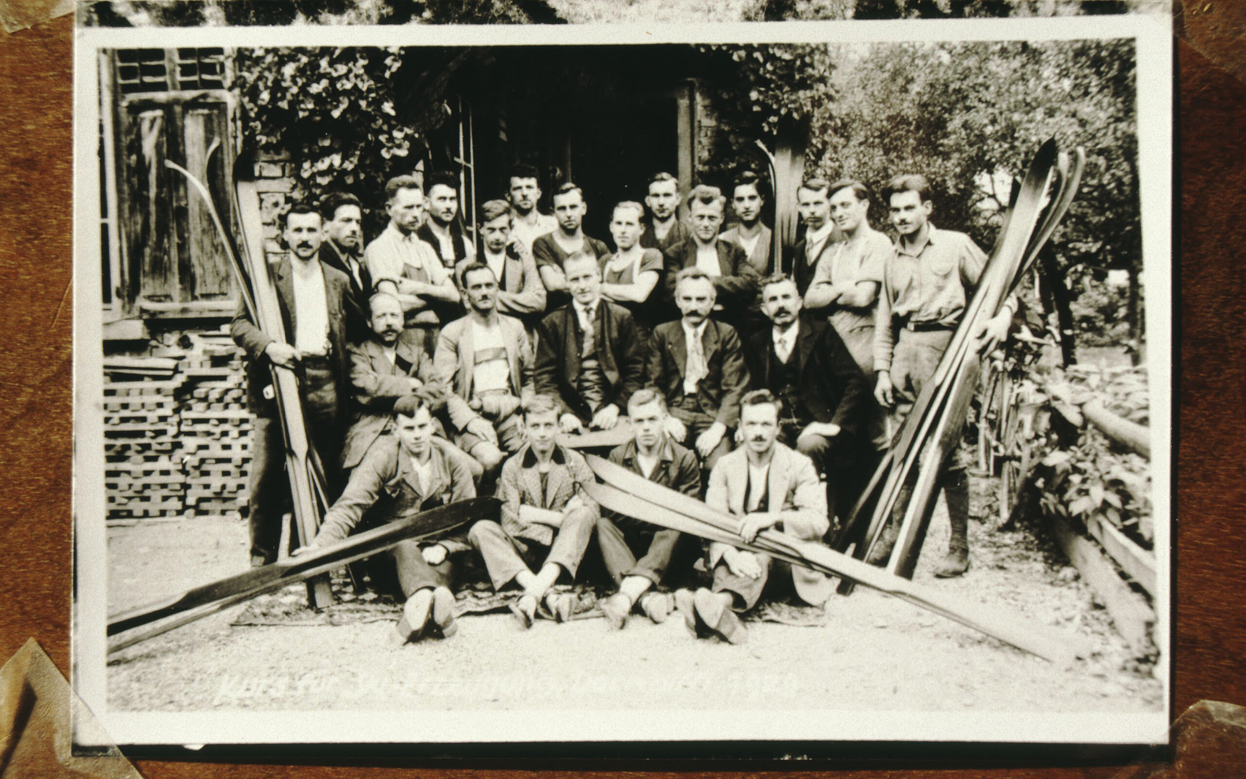Das Bild zeigt ein altes Foto von einer Gruppe von Männern mit selbstgebauten Schi.