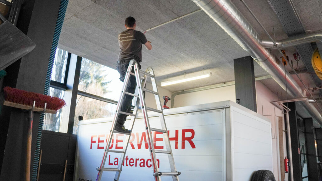 Das Bild zeigt einen Arbeiter auf einer Leiter bei der Montage einer Brandschutzanlage im Feuerwehrhaus in Lauterach.