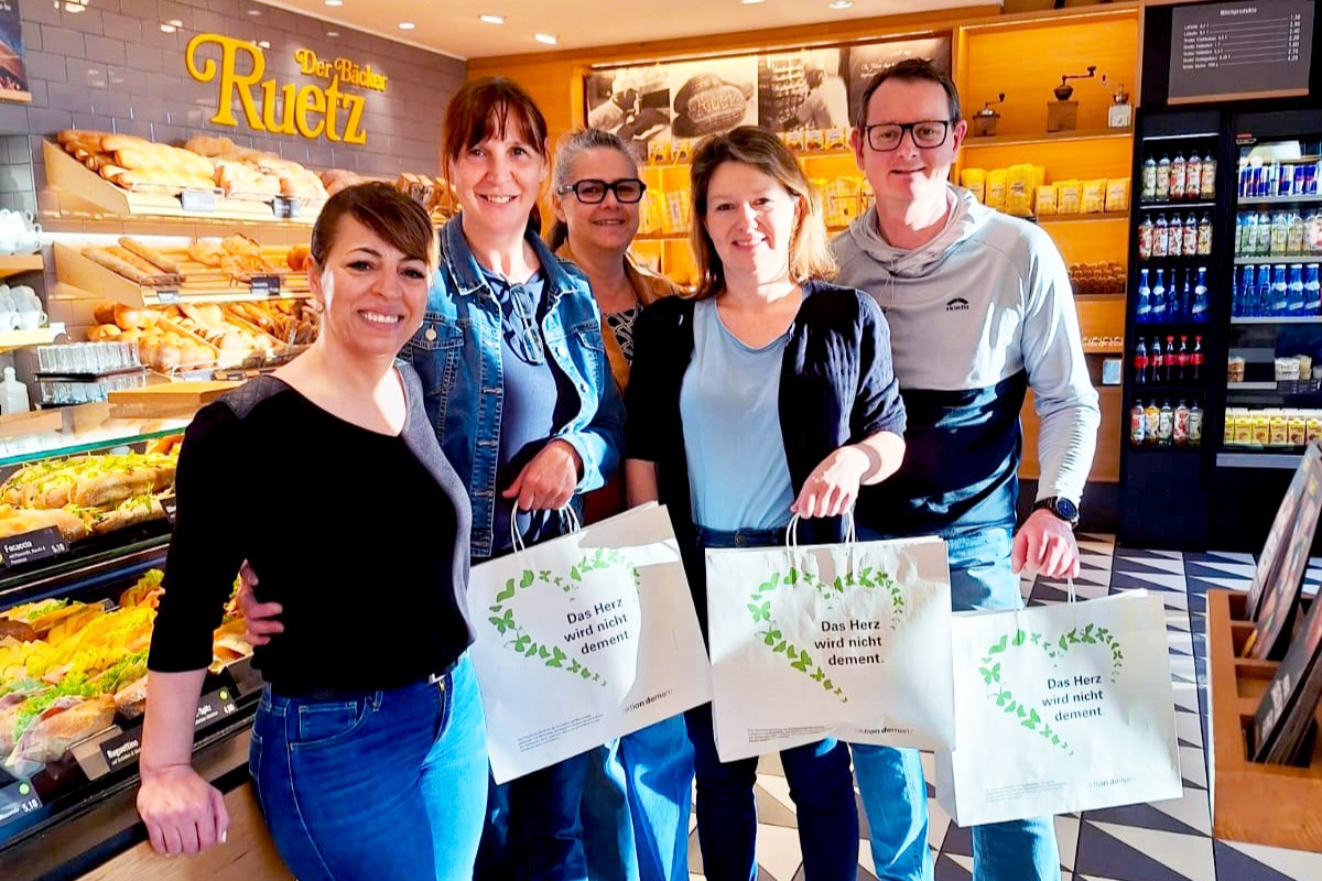 Das Bild zeigt fünf Personen in einer Bäckerei mit Papiertaschen mit der Aufschrift "Das Herz wird nicht dement".