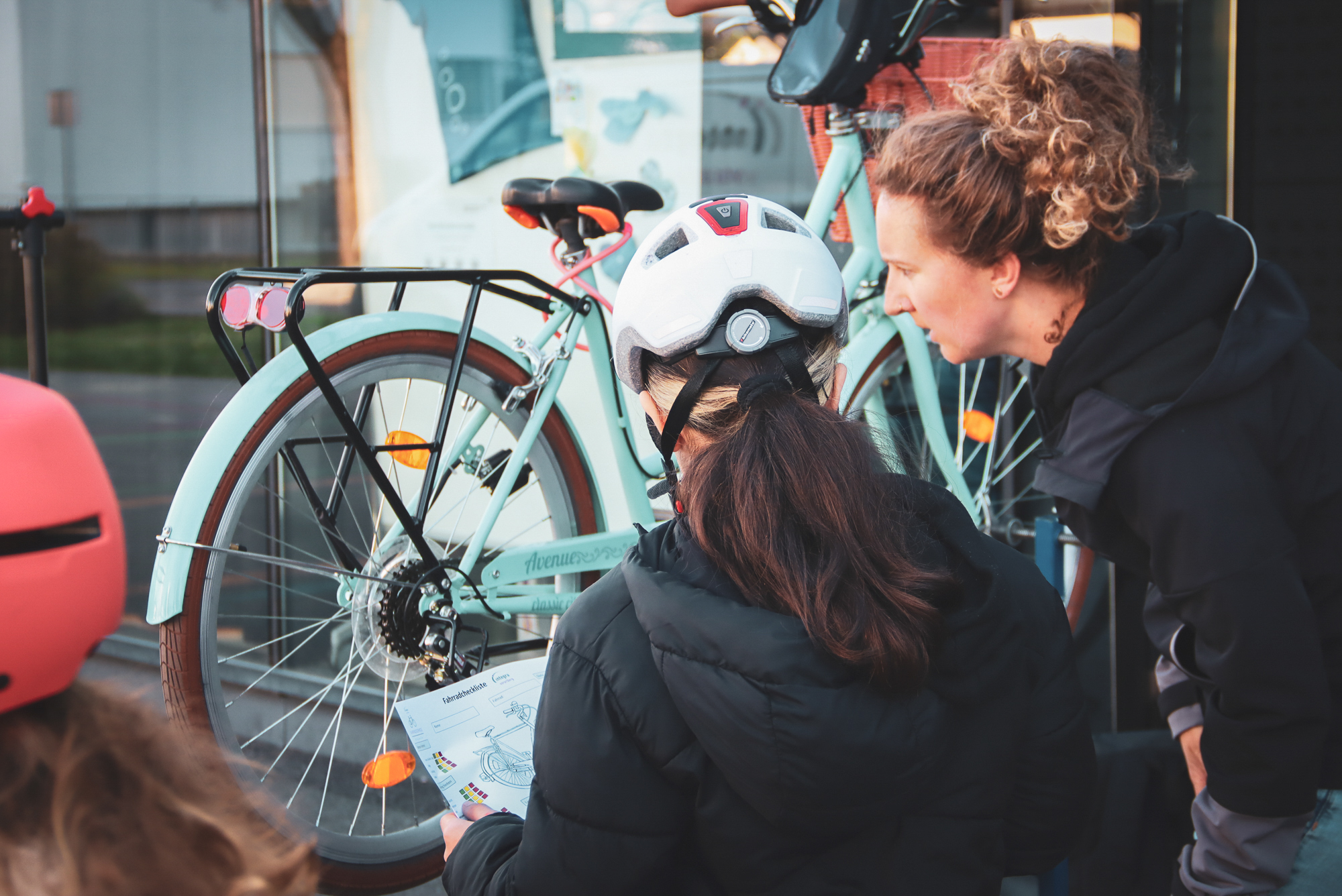 Das Bild zeigt zwei Personen von hinten, die mit einer Fahrradcheckliste an einem Fahrrad einen Rad-Check durchführen.