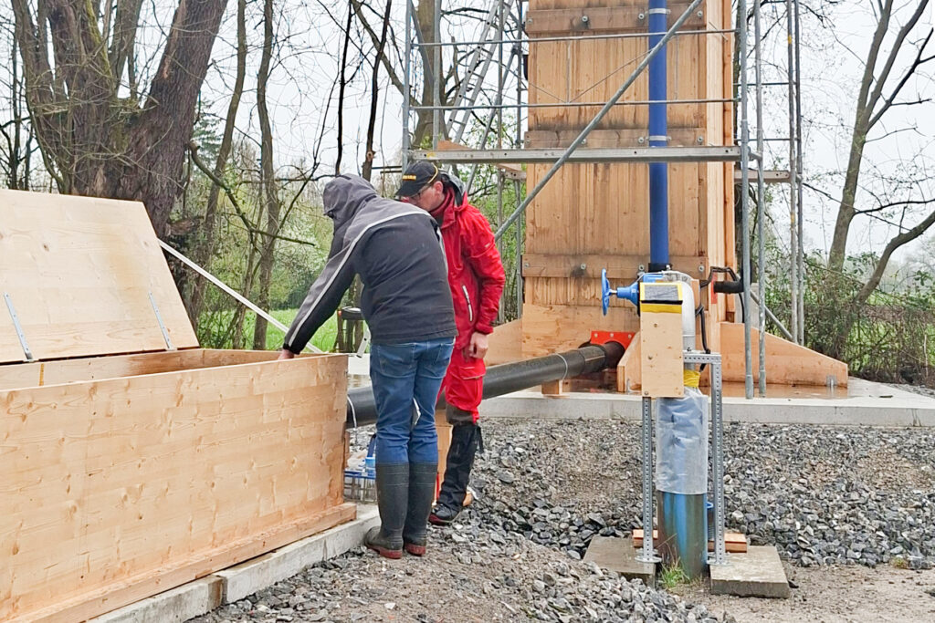 Das Bild zeigt zwei Personen, die bei einer Trinkwasser-Probebohrung in einen Schacht blicken.