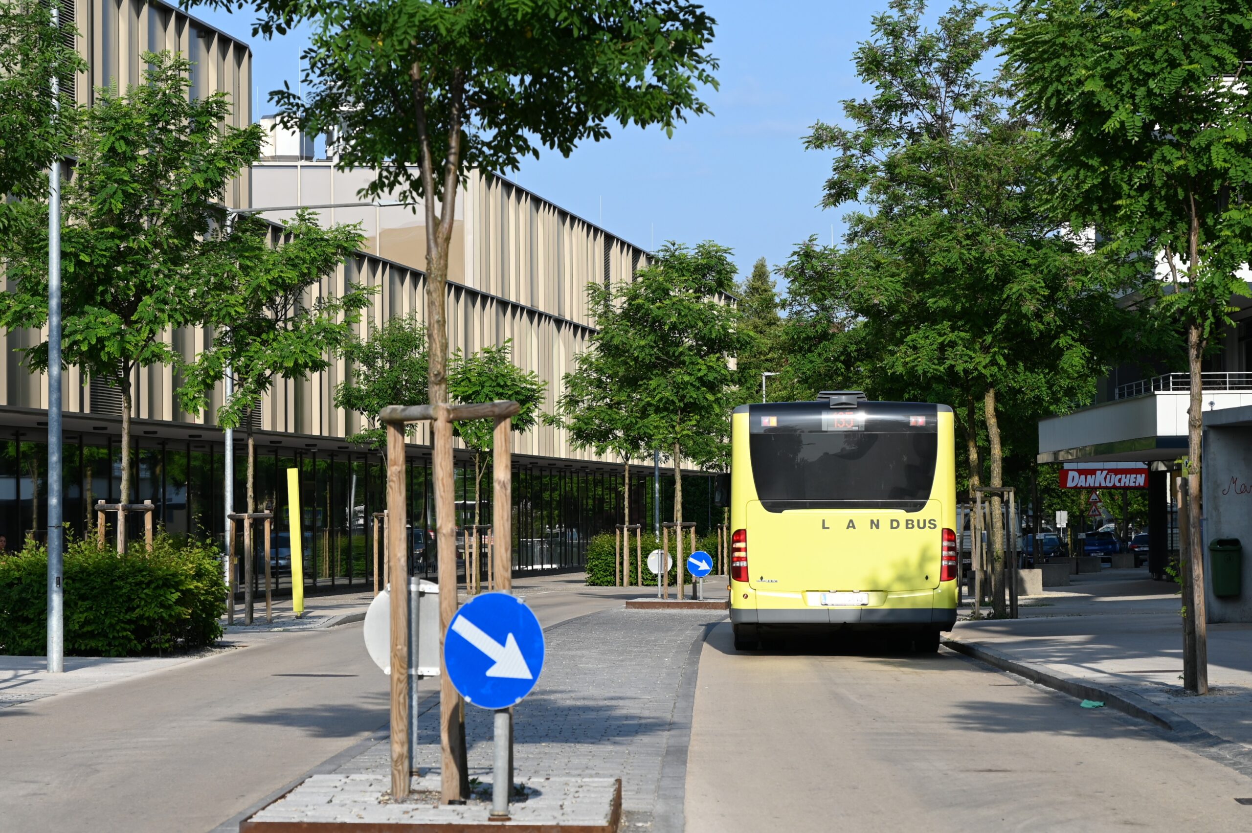 Das Bild zeigt einen Bus von hinten unter Bäumen an einer Bushaltestelle in der Karl-Höll-Straße in Lauterach.