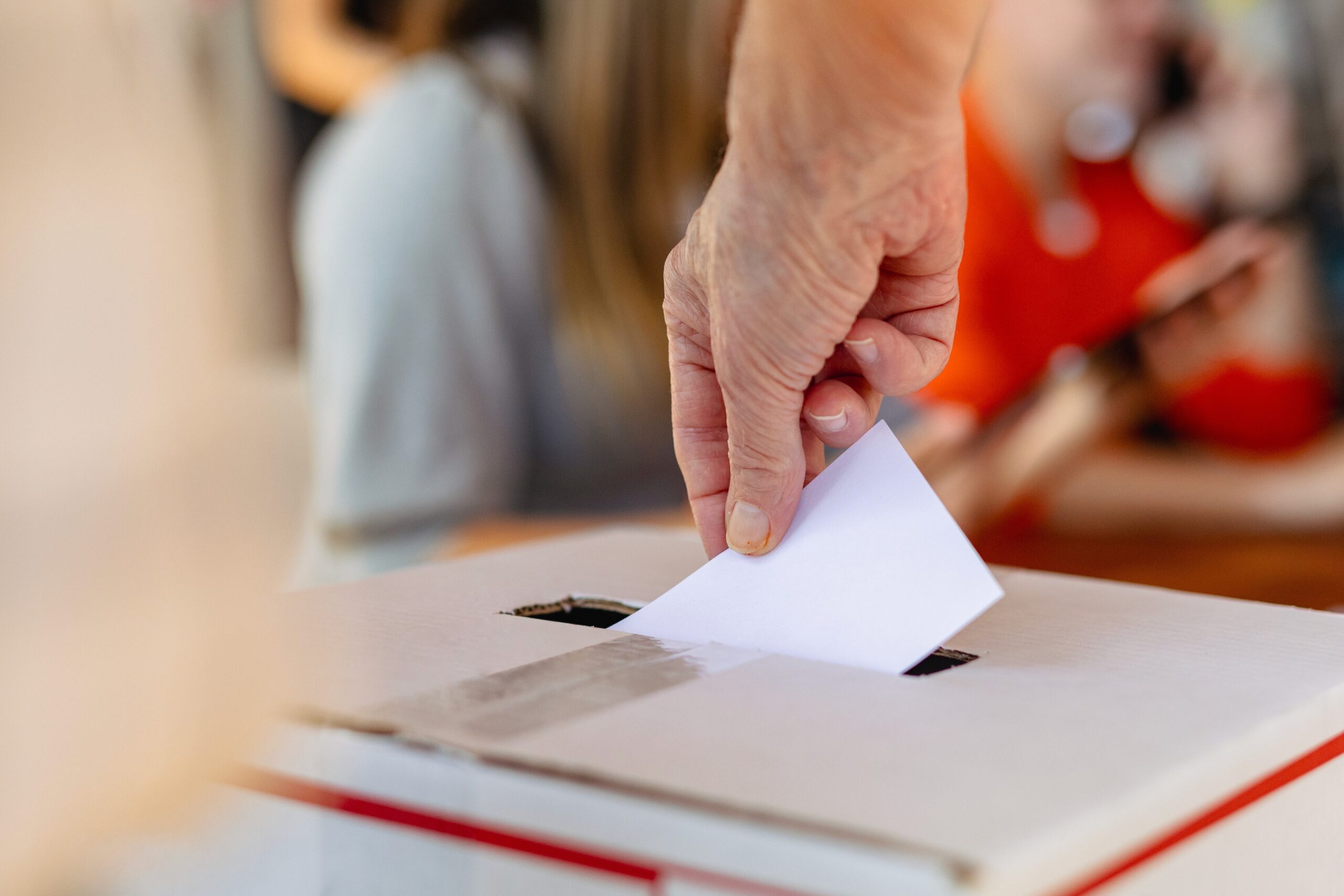 Das Bild zeigt die Hand einer Person, die einen Stimmzettel in eine Urne steckt.