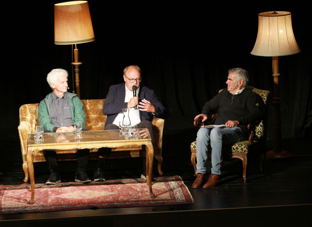 Auf dem Bild sieht man Dr. Hubert Dörler und Bürgermeister Elmar Rhomberg auf der Bühne des Vereinshauses sitzen. Gemeinsam mit Dr. Johannes Schmidle.