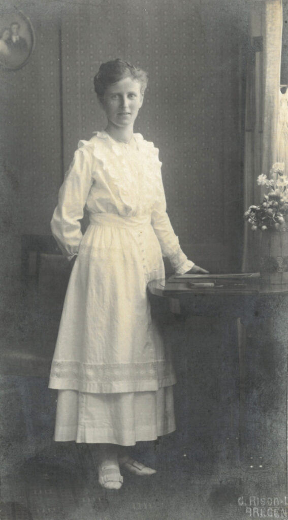 Historische Fotografie einer Frau in einem weißen Kleid, an einem Tisch stehend