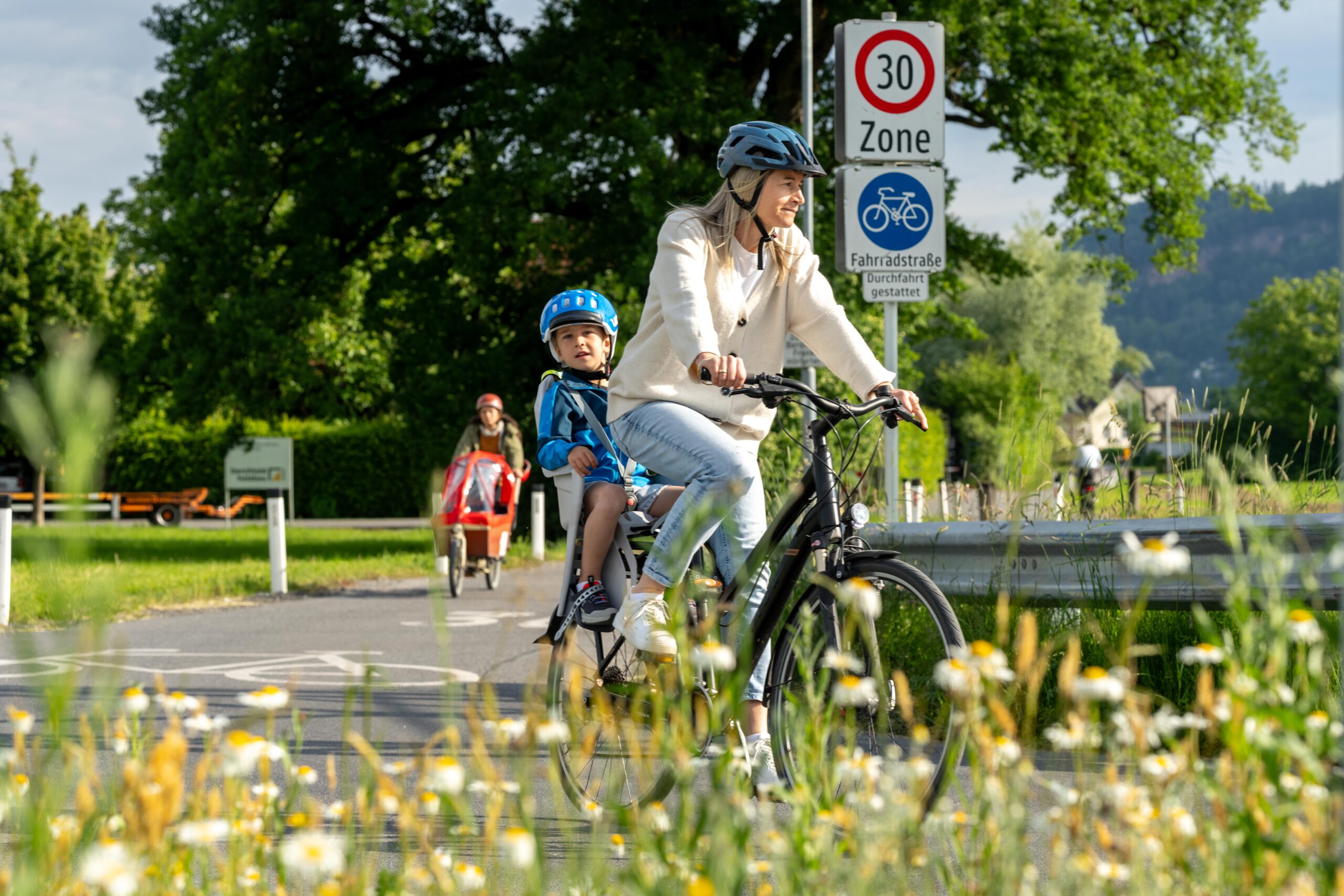 Frau fährt Fahrrad mit Kind im Kindersitz.