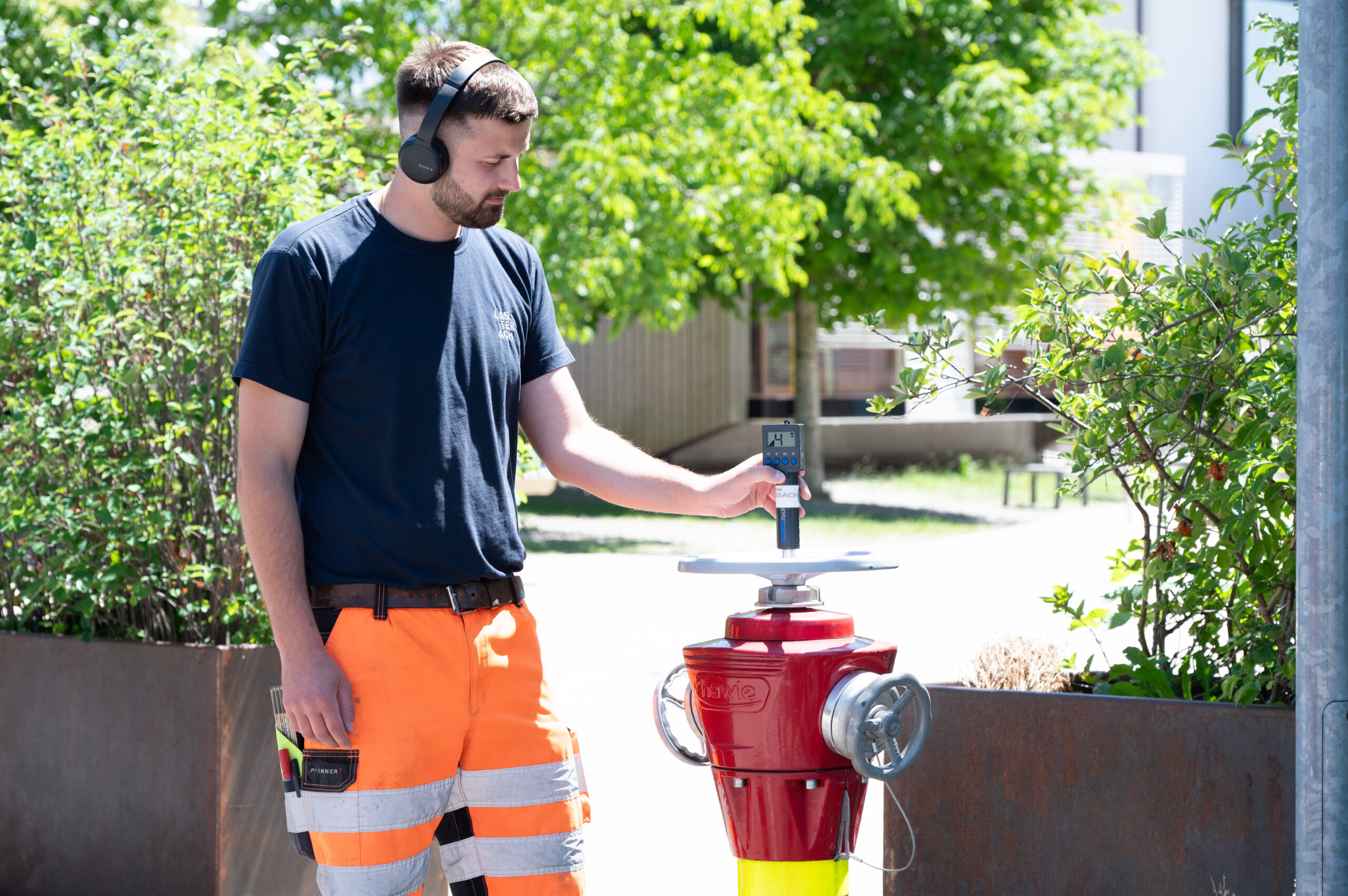 Ein Mann mit Kopfhörern und Arbeitskleidung hält ein Messgerät auf einen Wasserhydranten