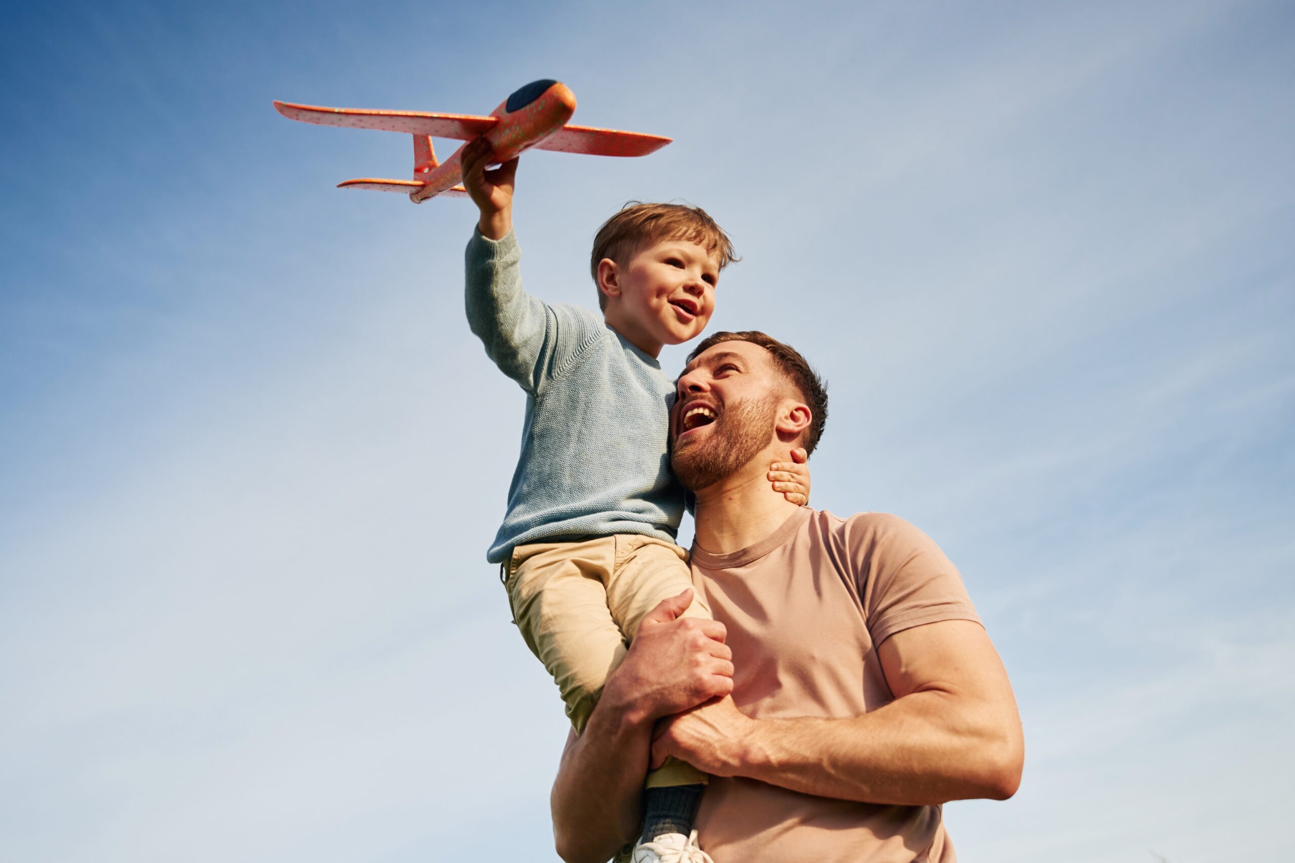 Ein Mann mit einem Kind auf dem Arm, das ein Spielzeugflugzeug in die Luft hält