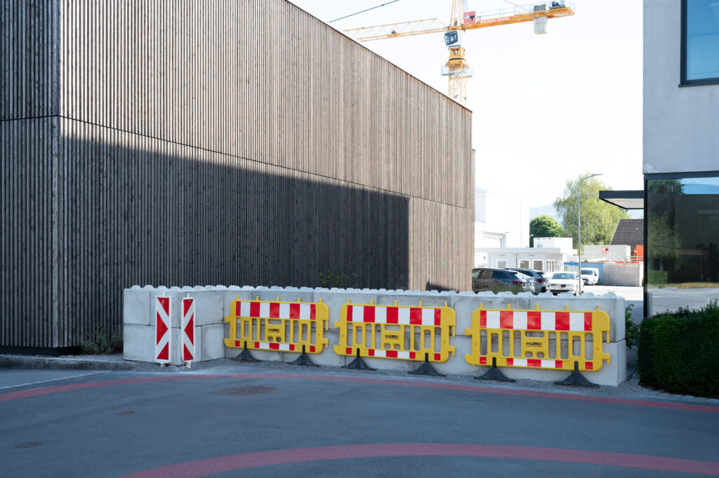 Absperrungen und Betonpfeiler vor einem Gebäude sowie ein Kran im Hintergrund