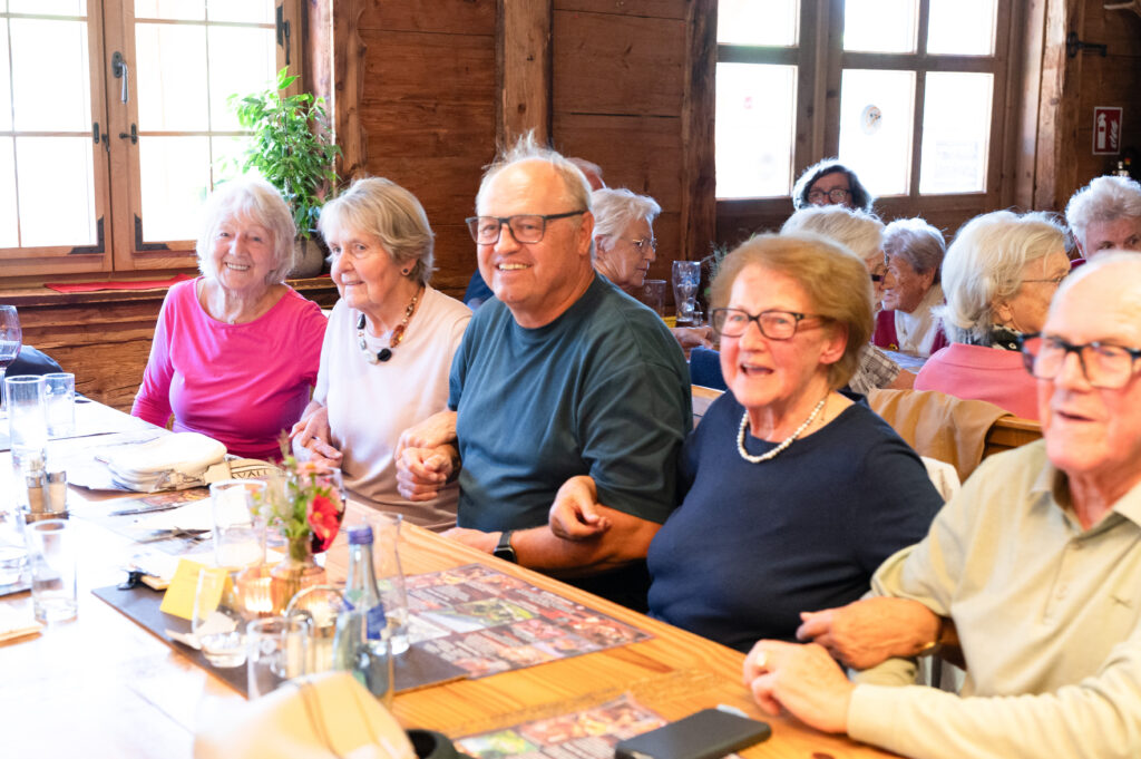Die Senior:innen und Elmar Rhomberg schunkeln und eine Frau singt dabei.