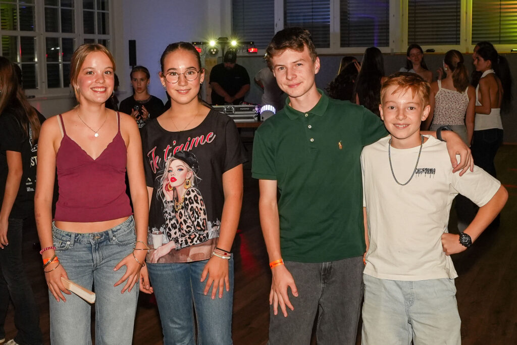 Vier Jugendliche stehen für das Foto nebeneinander und im Hintergrund sind andere Partygäste zu sehen.