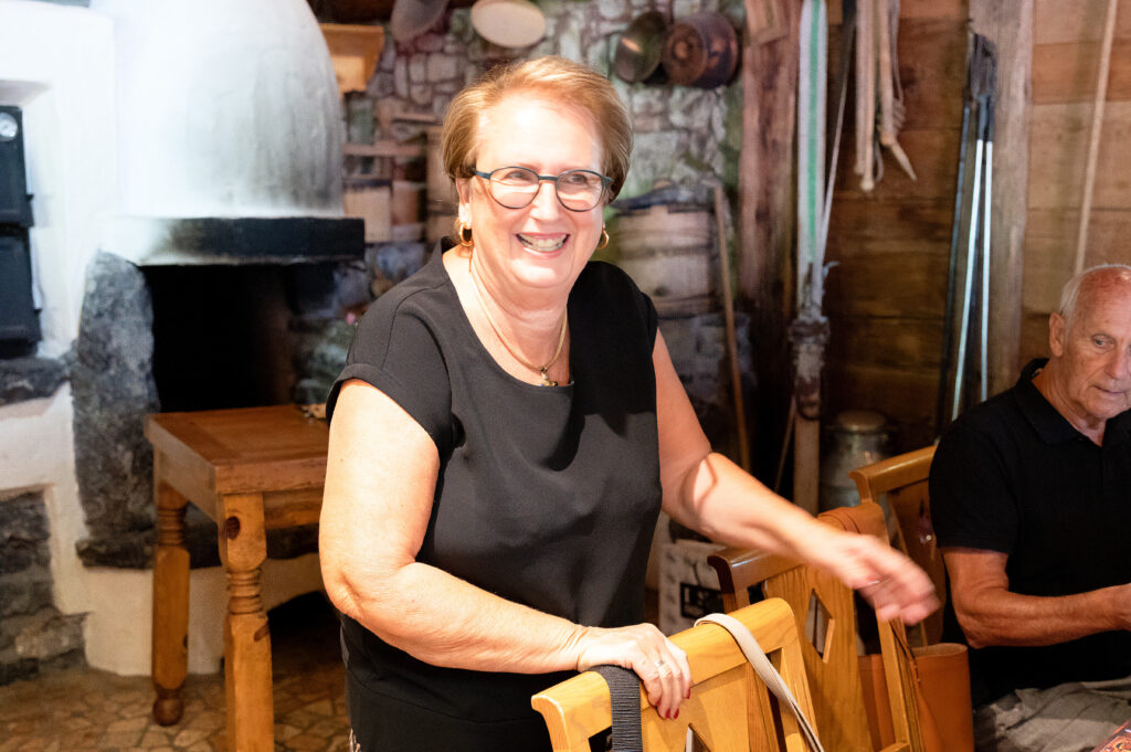 Doris Rohner hält sich an der Stuhllehne fest und steht dahinter und lacht.