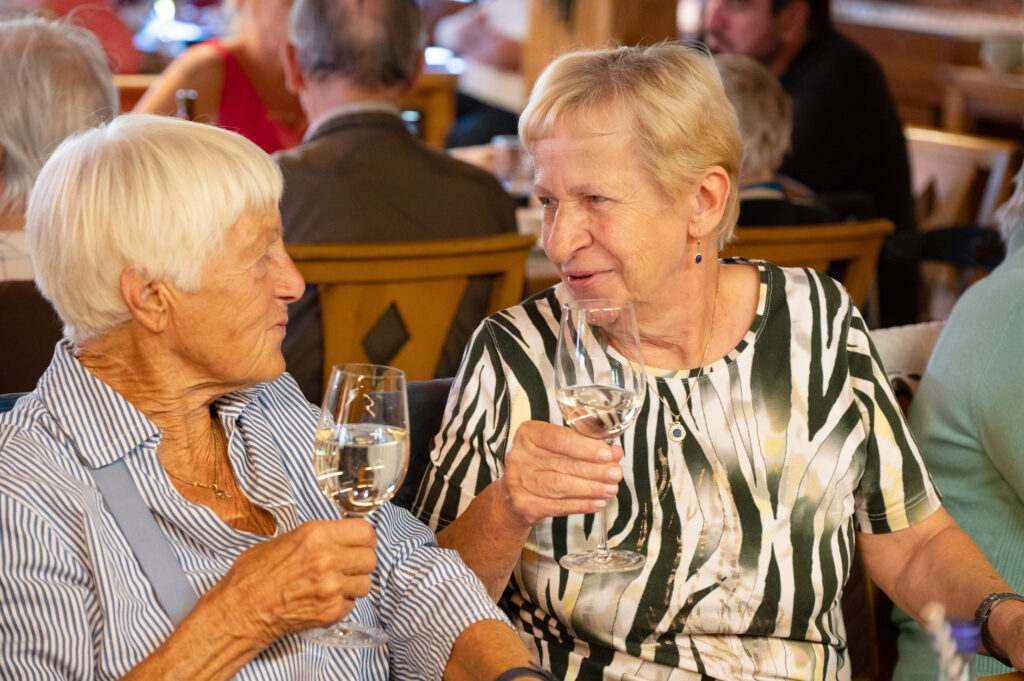 Zwei Seniorinnen schauen sich in die Augen und prosten sich mit Weingläser zu.