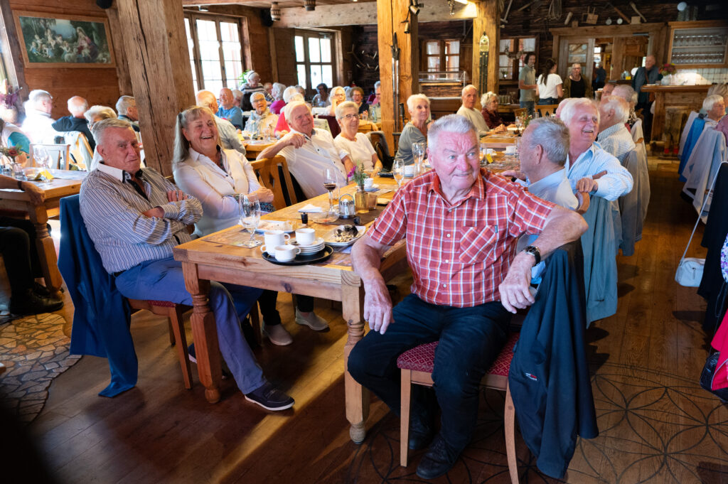 Die 144 Teilnehmer:innen sitzen an langen Tafeln in einem urigen Wirtshaus.