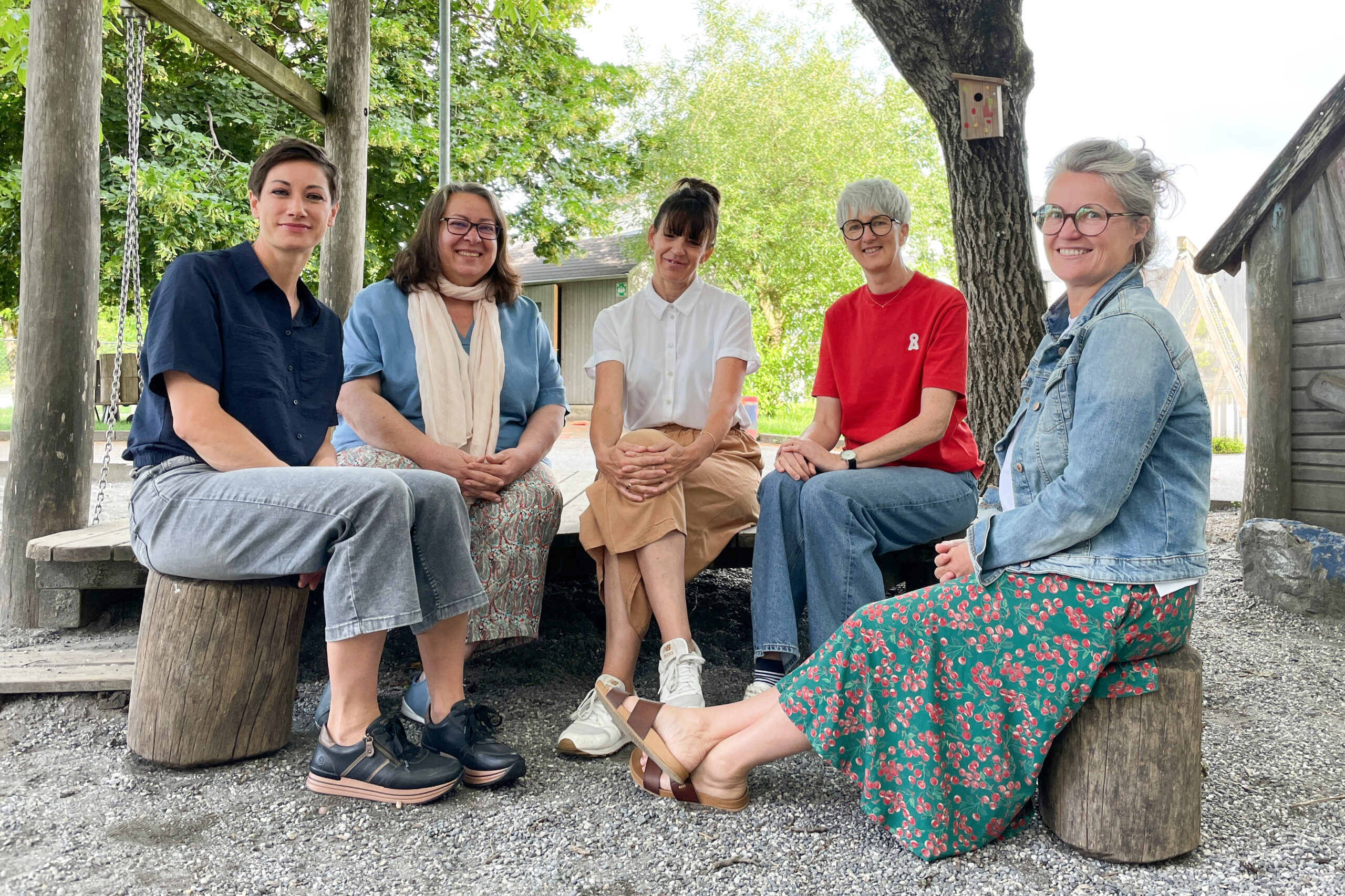 Fünf Frauen im Freien sitzend, in die Kamera lächelnd.