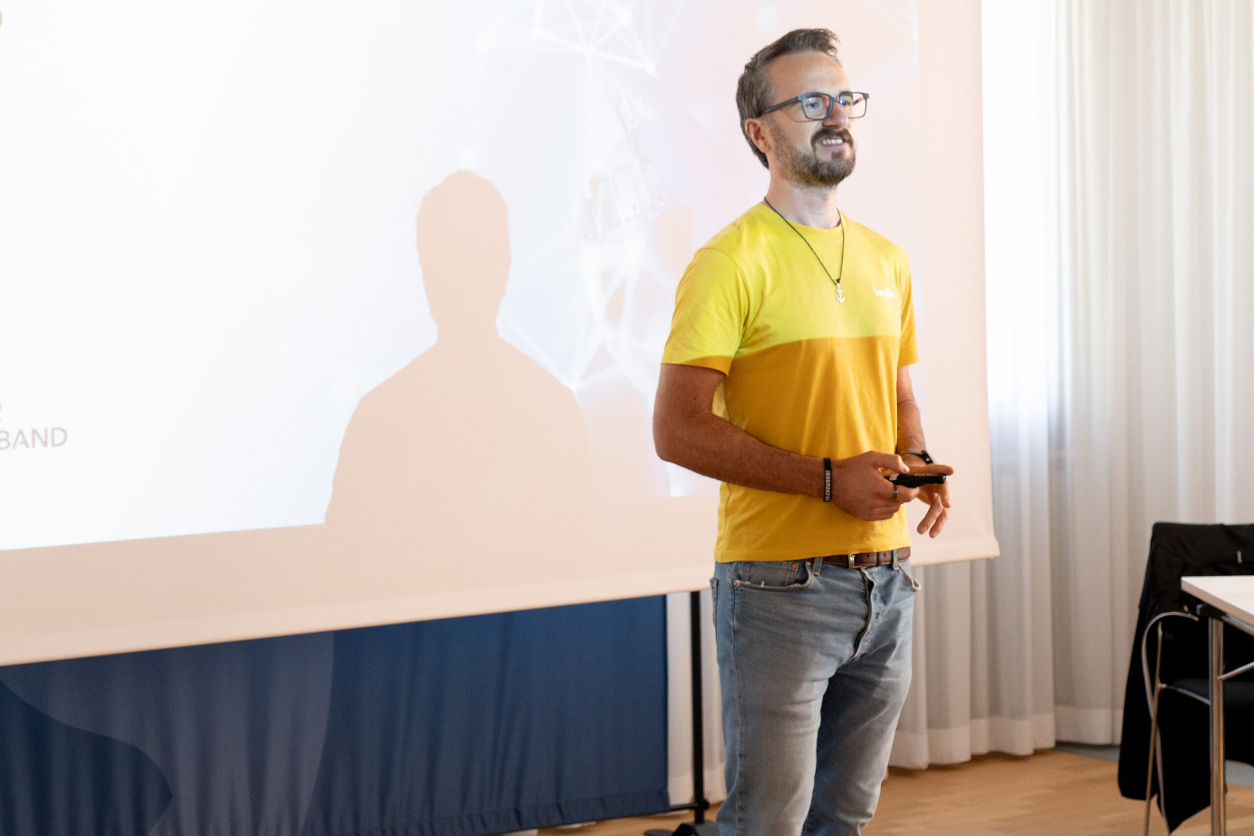 Mann mit Brille und gelbem T-Shirt hält Fernbedienung in der Hand