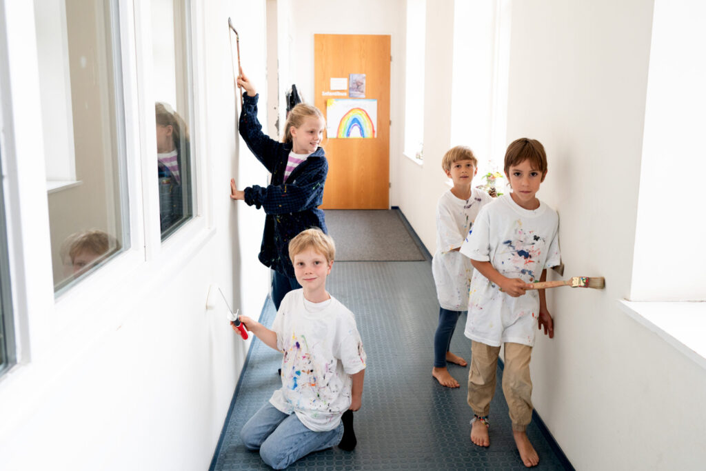Vier Kinder malen mit Pinseln die weiße Wände im Gang an