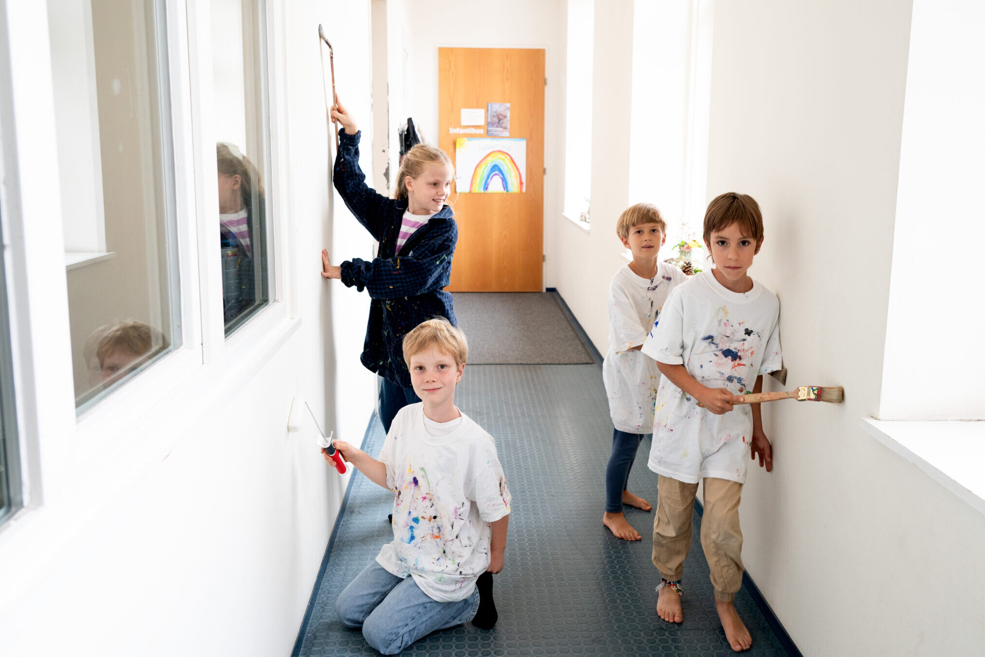 Vier Kinder malen mit Pinseln die weiße Wände im Gang an