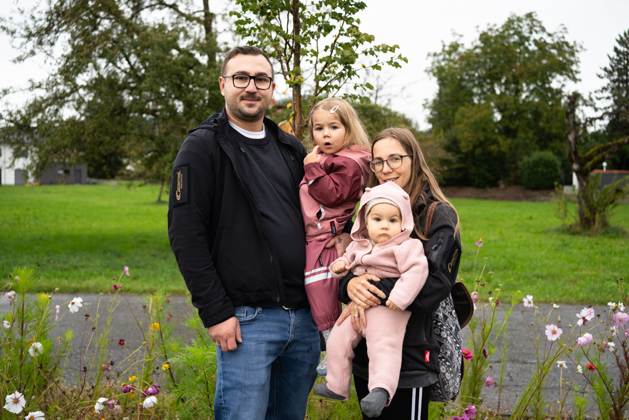 Familie mit zwei Kindern im Freien vor Bäumen und Blumen
